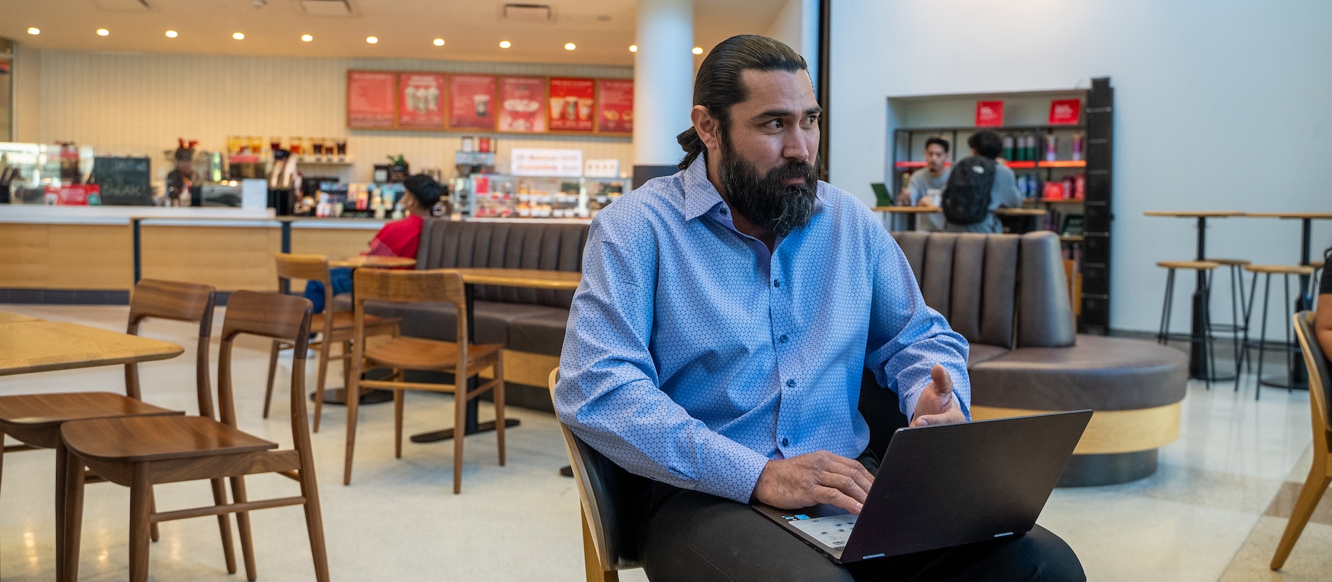 Student sitting down with laptop at coffee shop.