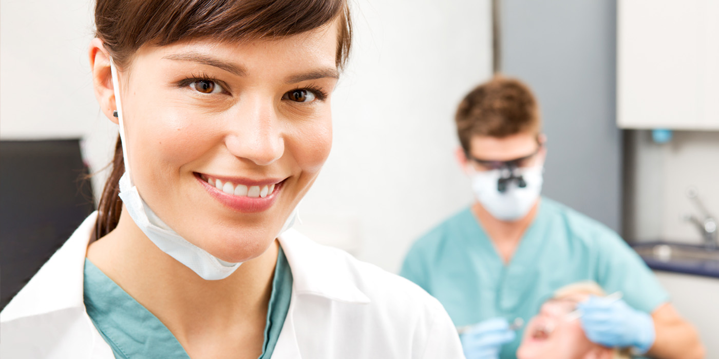 dental assistant smiling with dentist in background.